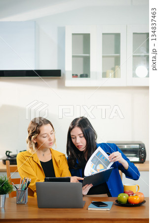 Two professional women collaborating on a business project with a laptop, notebook, and coffee at home. Two professional women collaborating on a business project with a laptop, notebook, and coffee at home. 134837463