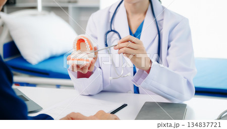 Dentist sitting at table with jaw samples tooth model and working with tablet and laptop in dental office professional dental clinic. Dentist sitting at table with jaw samples tooth model and working with tablet and laptop in dental office professional dental clinic. 134837721