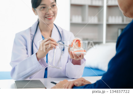 Dentist sitting at table with jaw samples tooth model and working with tablet and laptop in dental office professional dental clinic. 134837722