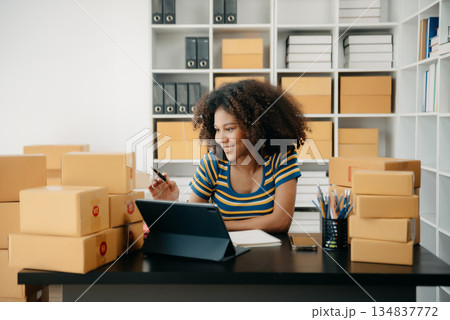 Startup small business SME, Entrepreneur owner African woman using smartphone or tablet taking receive and checking online purchase shopping order Startup small business SME, Entrepreneur owner African woman using smartphone or tablet taking receive and checking online purchase shopping order 134837772