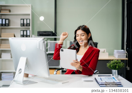 Asian woman using laptop and tablet while sitting at her working place. Concentrated Asian woman using laptop and tablet while sitting at her working place. Concentrated 134838101