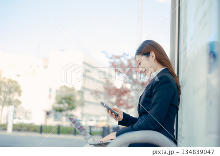 バス停でパソコンとスマホを使う日本人女子大学生 134839047