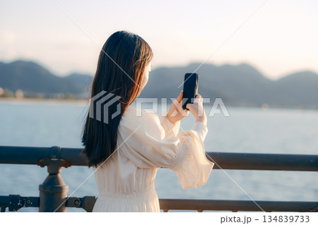 海を背景に堤防でスマホを見る日本人女性 134839733
