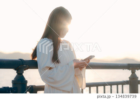 海を背景に堤防でスマホを見る日本人女性 134839739