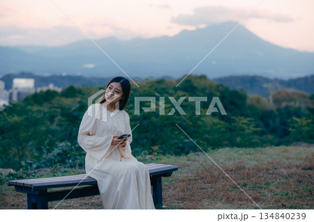 街並みを望む高台でスマートフォンを見る日本人女性 134840239