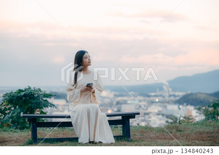 街並みを望む高台でスマートフォンを見る日本人女性 134840243