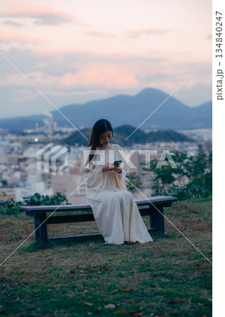 街並みを望む高台でスマートフォンを見る日本人女性 街並みを望む高台でスマートフォンを見る日本人女性 134840247