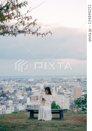街並みを望む高台でスマートフォンを見る日本人女性 134840251