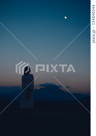 月が浮かぶ夕暮れの山で佇む女性のシルエット 134840344