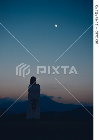月が浮かぶ夕暮れの山で佇む女性のシルエット 134840345