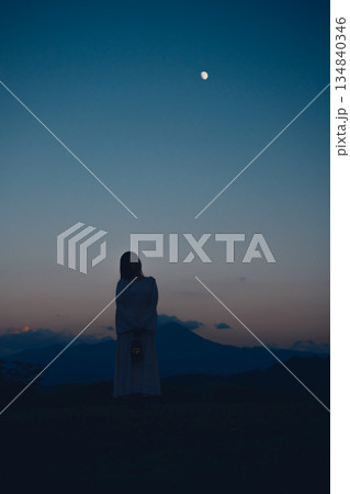 月が浮かぶ夕暮れの山で佇む女性のシルエット 134840346