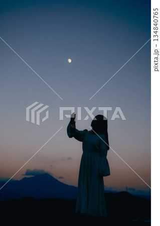 月が浮かぶ夕暮れの山で佇む女性のシルエット 月が浮かぶ夕暮れの山で佇む女性のシルエット 134840765