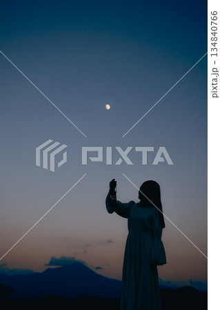 月が浮かぶ夕暮れの山で佇む女性のシルエット 134840766