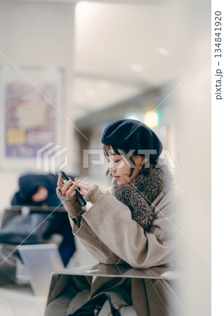 座ってスマートフォンを操作しながら待ち合わせをする30代女性 134841920
