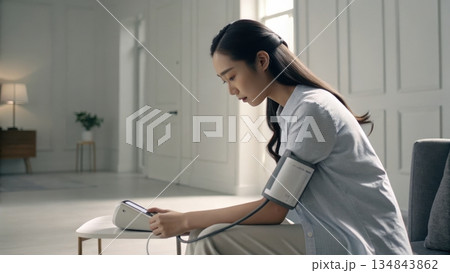 Young woman measuring blood pressure at home with a digital device 134843862