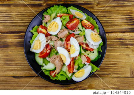 Tasty tuna salad with eggs, lettuce and fresh vegetables on wooden table. Top view 134844010