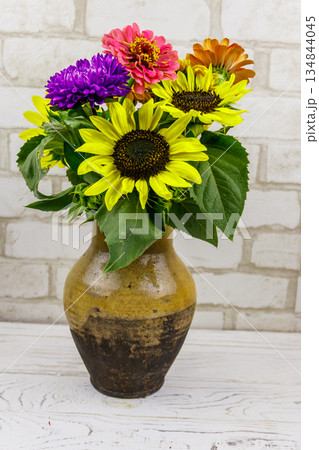Bouquet of flowers in antique rustic clay jug against white brick wall Bouquet of flowers in antique rustic clay jug against white brick wall 134844045