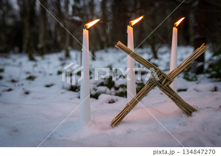 Blessed Imbolc greeting card. Brigid cross of straw and candles. Winter forest nature background. symbol of Imbolc Blessed Imbolc greeting card. Brigid cross of straw and candles. Winter forest nature background. symbol of Imbolc 134847270