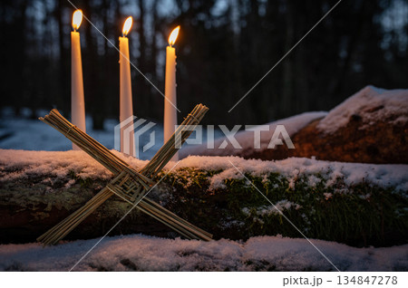 Blessed Imbolc greeting card. Brigid cross of straw and candles. Winter forest nature background. symbol of Imbolc 134847278