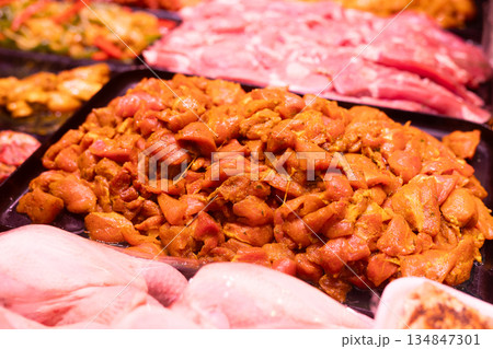 Marinated chicken pieces in curry are displayed in display case. Butcher shop sells fresh meat products, semi-finished products 134847301