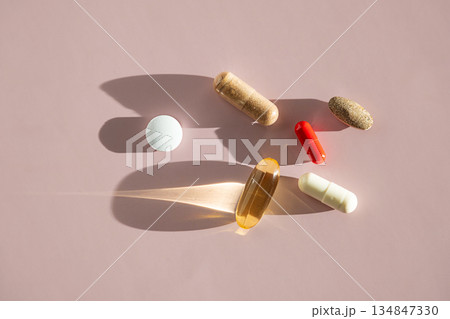 Various vitamin and supplement pills in different colors and shapes on pink surface. Various vitamin and supplement pills in different colors and shapes on pink surface. 134847330