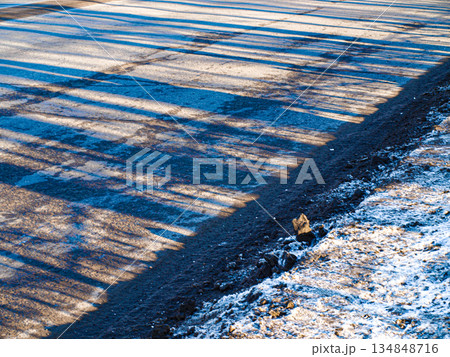 Spring thaw, a road with snow and purple transparent shadows with a fine stripe. Roadside, diagonal composition Spring thaw, a road with snow and purple transparent shadows with a fine stripe. Roadside, diagonal composition 134848716