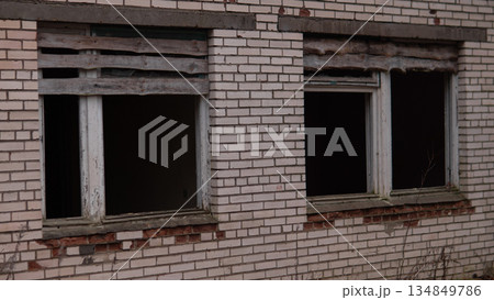 Two broken windows are visible on an old brick building in an empty space. The wood framing around the windows shows signs of decay in the late afternoon light. Two broken windows are visible on an old brick building in an empty space. The wood framing around the windows shows signs of decay in the late afternoon light. 134849786