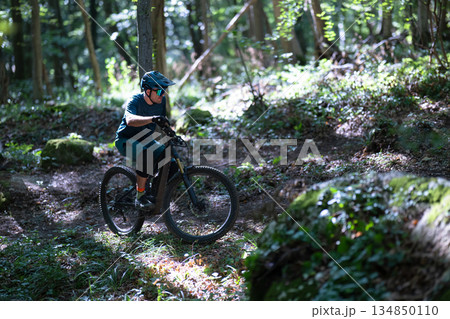 Man rides electric mountain bike through forest trail wearing helmet and protective gear 134850110