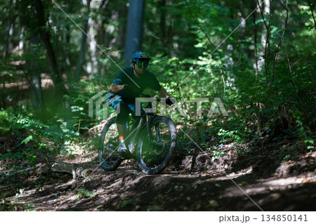 Rider on an electric mountain bike navigating a forest trail in sunlight Rider on an electric mountain bike navigating a forest trail in sunlight 134850141