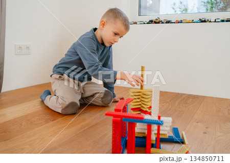 Young child sitting on the floor and assembling colorful building blocks. Calm home environment and focused play highlight themes of childhood development, creativity, motor skills and learning Young child sitting on the floor and assembling colorful building blocks. Calm home environment and focused play highlight themes of childhood development, creativity, motor skills and learning 134850711