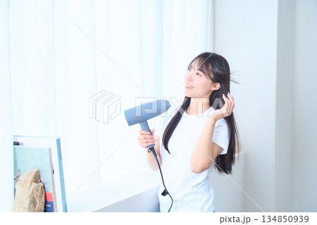 明るいリビングでドライヤーを使う日本人女性 明るいリビングでドライヤーを使う日本人女性 134850939