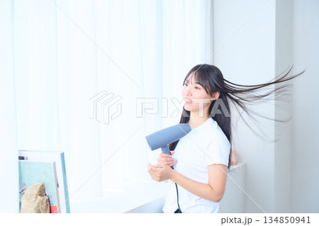 明るいリビングでドライヤーを使う日本人女性 明るいリビングでドライヤーを使う日本人女性 134850941