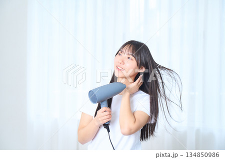 明るいリビングでドライヤーを使う日本人女性 明るいリビングでドライヤーを使う日本人女性 134850986
