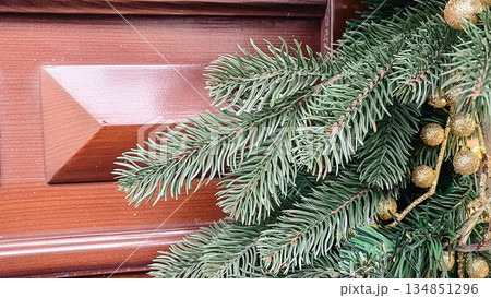Close-up of green spruce branches with golden decorative berries on a brown wooden door background Close-up of green spruce branches with golden decorative berries on a brown wooden door background 134851296