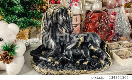 Black and gold horse with foal figurine on a store shelf surrounded by festive Christmas decorations Black and gold horse with foal figurine on a store shelf surrounded by festive Christmas decorations 134851565