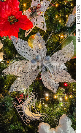 Close-up of a decorated Christmas tree with a large silver mesh flower, white ornamental sleigh, and warm glowing lights. Close-up of a decorated Christmas tree with a large silver mesh flower, white ornamental sleigh, and warm glowing lights. 134851570