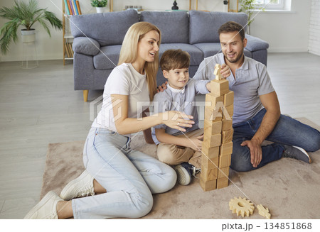 Young family with a child son playing an educational wooden pyramid game at home together. Young family with a child son playing an educational wooden pyramid game at home together. 134851868
