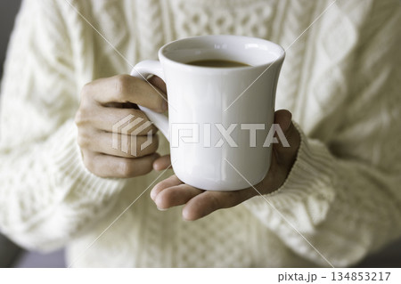 ニットを着た人物が白いマグカップのホットコーヒーを両手で持つ手元(クローズアップ) ニットを着た人物が白いマグカップのホットコーヒーを両手で持つ手元(クローズアップ) 134853217