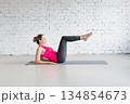 Modified Boat Pose with bent knees, elbows back. Fit Caucasian woman practice yoga indoor in loft studio. 134854673
