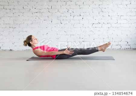 Yoga, Half Boat pose. Fit Caucasian woman practice Ardha Navasana exercise indoor in loft studio. 134854674