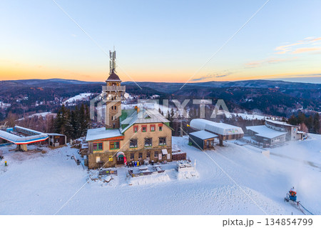 Tanvaldsky Spicak Ski Resort shows the lookout tower surrounded by snow. People enjoy winter activities as the sun sets over the mountains in Czechia. The resort has several buildings and chairlifts. Tanvaldsky Spicak Ski Resort shows the lookout tower surrounded by snow. People enjoy winter activities as the sun sets over the mountains in Czechia. The resort has several buildings and chairlifts. 134854799