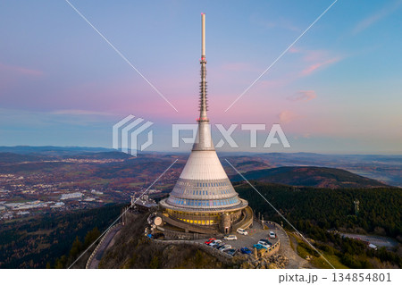 Jested mountain hotel during sunset. The drone view captures the hotel and surrounding landscape in Liberec. The sky glows with evening colors. 134854801