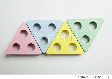Minimalist pastel colored wooden triangle shapes with three drilled holes arranged on a white background. A simple still life suitable for childhood, learning, and creative play 134855084