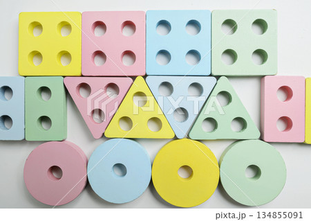 Top view of assorted wooden shape sorter toys in pastel colors, arranged in a circle on a white surface. The shapes include squares, circles, and triangles Top view of assorted wooden shape sorter toys in pastel colors, arranged in a circle on a white surface. The shapes include squares, circles, and triangles 134855091