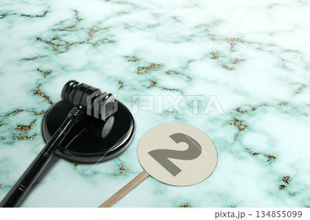 Black gavel resting on its stand next to a paddle with the number two on a light marble background. Ideal for concepts of law, auctions, or legal processes Black gavel resting on its stand next to a paddle with the number two on a light marble background. Ideal for concepts of law, auctions, or legal processes 134855099