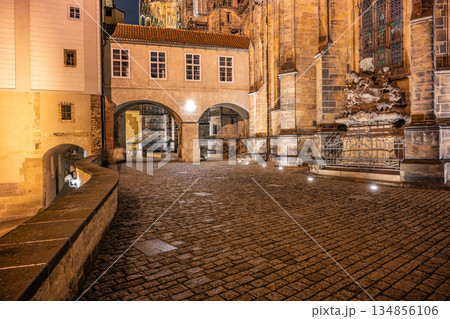 The covered bridge next to Saint Vitus Cathedral illuminates the cobblestone path in Prague Castle at night, showcasing the historic architecture under soft street lighting. The covered bridge next to Saint Vitus Cathedral illuminates the cobblestone path in Prague Castle at night, showcasing the historic architecture under soft street lighting. 134856106