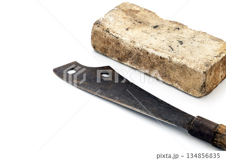 A big thick whetstone rests near a rusty machete on a white surface. 134856835