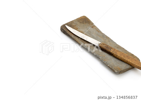 A knife with a wooden handle lays atop a gray sharpening stone, angled in the top right corner of the frame. 134856837