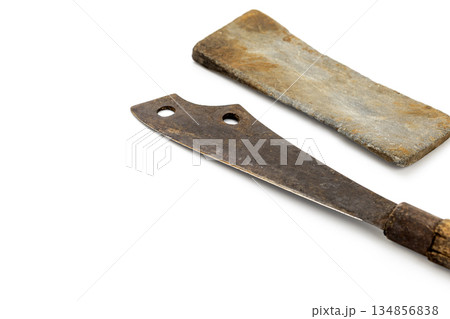 On white, a vintage rusty cleaver with a wooden handle lies next to a sharpening stone. Both show signs of age. On white, a vintage rusty cleaver with a wooden handle lies next to a sharpening stone. Both show signs of age. 134856838