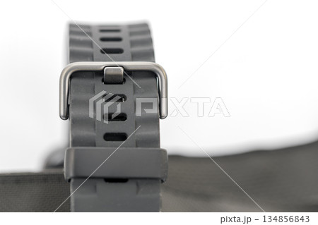 Close-up of a dark gray textured watch band with a metal buckle, against a blurred white background. Close-up of a dark gray textured watch band with a metal buckle, against a blurred white background. 134856843